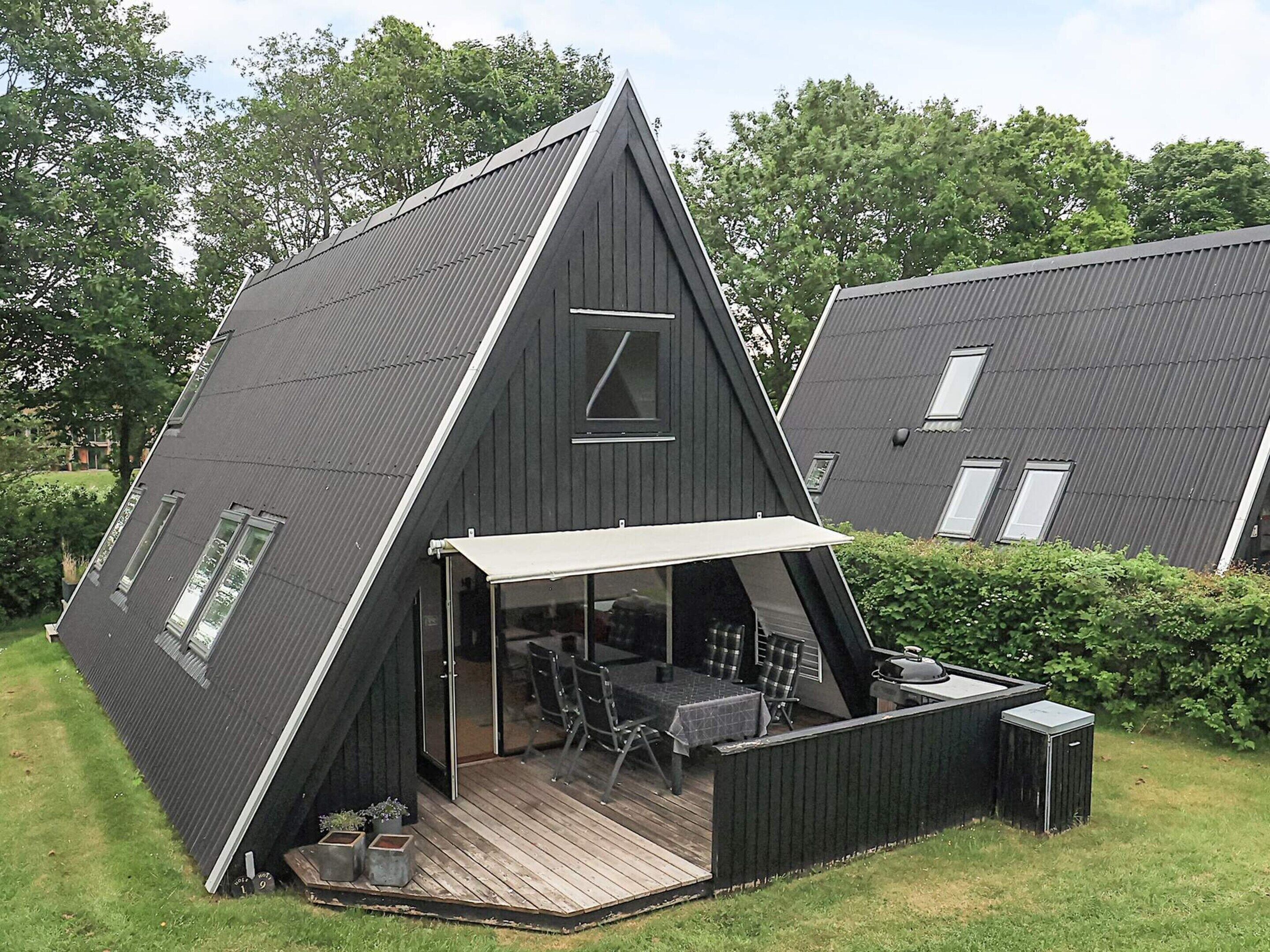 Een driekantig huis met een terras, buitenmeubels en een barbecueplek.