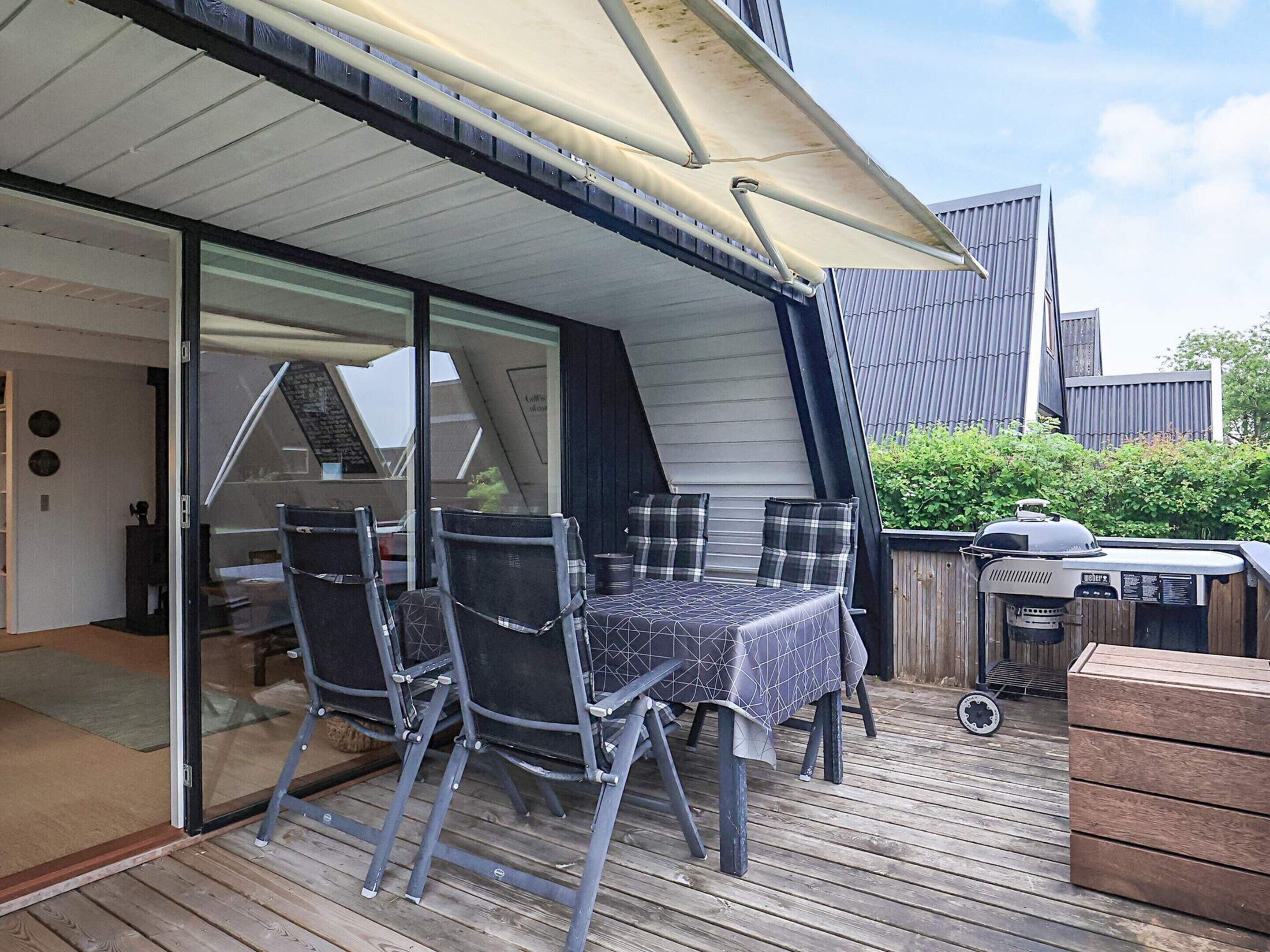 An outdoor patio with a table and chairs, a barbecue grill, and a wooden deck.