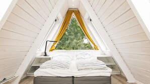 A triangular attic bedroom with a bed, a desk, and a window with yellow curtains. - 4 Star Holiday Home in Farso (Farso)