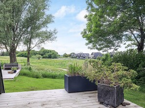 A wooden deck with potted plants, a grassy field, and houses in the background. - 4 Star Holiday Home in Farso (Farso)