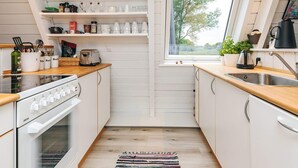 A kitchen with white cabinets, a wooden countertop, a stove, a toaster, and a window with a view of trees. - 4 Star Holiday Home in Farso (Farso)