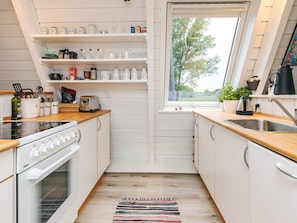 A kitchen with white cabinets, a wooden countertop, a stove, a toaster, and a window with a view of trees. - 4 Star Holiday Home in Farso (Farso)