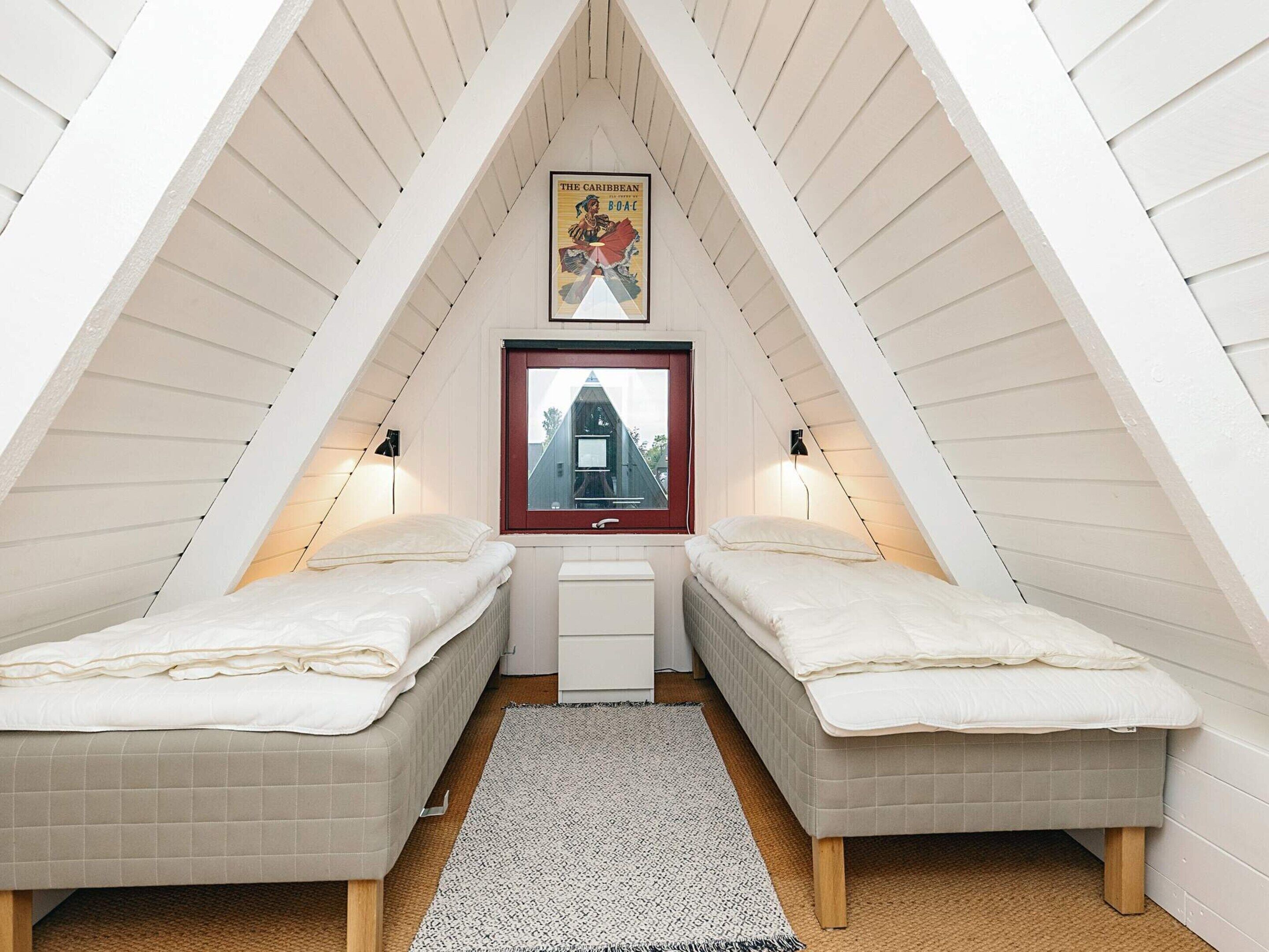 Un dormitorio en ático pequeño con dos camas, una ventana, una mesita de noche y un cartel en la pared.