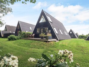 A modern, triangular house with a large glass window, surrounded by a well-maintained lawn and greenery. - 4 Star Holiday Home in Farso (Farso)