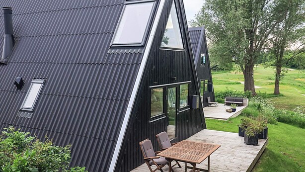 A modern house with a sloped roof, large windows, and a deck with outdoor furniture. - 4 Star Holiday Home in Farso (Farso)