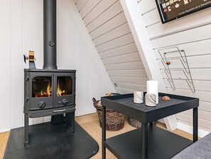Une pièce moderne avec un poêle à bois noir, une petite table avec des bougies et un téléviseur fixé au mur.