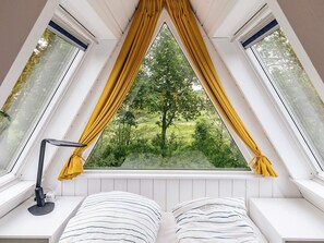 A room with a sloped ceiling, a bed with striped bedding, a desk with a lamp, and a window with yellow curtains. - 4 Star Holiday Home in Farso (Farso)