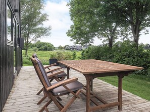 Une terrasse en bois avec une table et quatre chaises, donnant sur un espace verdoyant agrémenté d’arbres et de maisons.