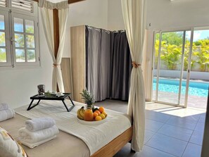 Ein Schlafzimmer mit einem Bett, einem Tablett mit Früchten und Getränken, einem Fenster und Blick auf einen Swimmingpool.