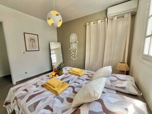 Ein Schlafzimmer mit Bett, Nachttisch, Lampe, Traumfänger und einer Wand-Klimaanlage.