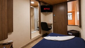 Habitació amb llit, escriptori, cadira, televisió que mostra 'NETFLIX' i finestra.