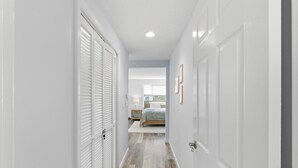 Un couloir avec des portes blanches, un lit recouvert d’une couverture bleue et un plancher en bois.