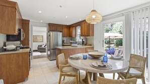 Une cuisine moderne avec des meubles en bois, un réfrigérateur en acier inoxydable et un coin repas comprenant des chaises en osier et une table ronde.