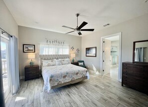 Ein Schlafzimmer mit einem Bett, einem Deckenventilator, einem Nachttisch, einer Kommode und einer Tür zu einem Badezimmer.