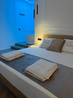 Habitación de hotel con cama, dos toallas, mesita de noche y una lámpara de pared.