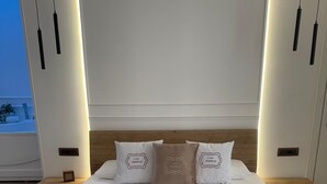 Un lit bien fait, avec du linge de lit blanc et une serviette enroulée, une tête de lit en bois et des tables de chevet avec des lampes.