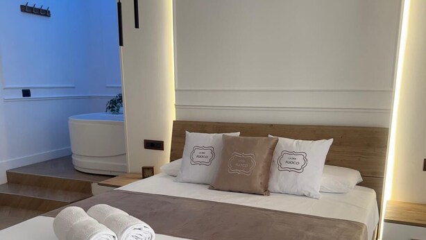 Une chambre d’hôtel moderne avec un lit en bois, du linge de lit blanc et un plafond éclairé d’une lumière bleue.