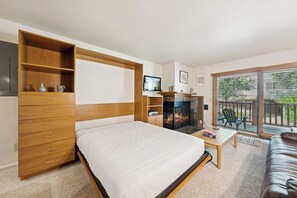 Ein Schlafzimmer mit Bett, Holzkommode, Fernseher, Kamin und einem Balkon mit Sitzmöbeln.