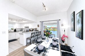 A modern kitchen with white cabinets, a dining area with a checkered tablecloth, and a view of a lake. - Stylish Lake View House: Minutes to Beaches & IMG, Pet-friendly (Bradenton)