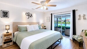 A bedroom with a bed, bedside tables, a ceiling fan, a view of a swimming pool, and a balcony with a chair. - Stylish Lake View House: Minutes to Beaches & IMG, Pet-friendly (Bradenton)