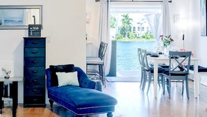 A modern living room with a blue sofa, a dining area with white chairs, and a view of a body of water. - Stylish Lake View House: Minutes to Beaches & IMG, Pet-friendly (Bradenton)