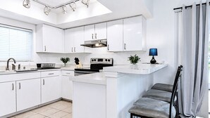 A modern kitchen with white cabinetry, a built-in stove, and a dining area with a grey bench. - Stylish Lake View House: Minutes to Beaches & IMG, Pet-friendly (Bradenton)