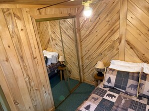 A wooden-paneled room with a bed, a nightstand, a lamp, and a mirror.