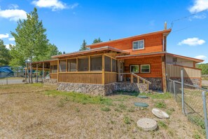 A two-story wooden house with a stone foundation, a covered porch, and a fenced yard. - Alpine Dream | ATV, Fishing & Mountain Escape (South Fork)