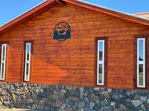 A wooden building with a stone foundation, a logo with a mountain and elk, and three windows.