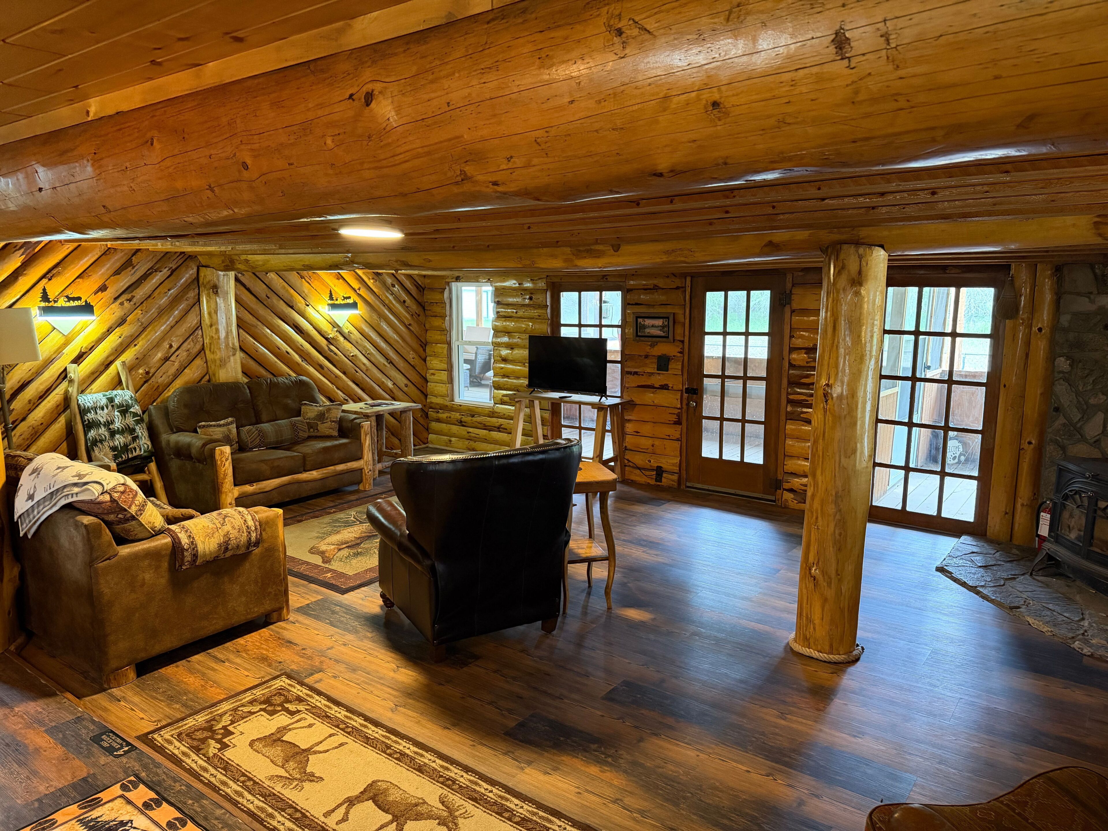 L’intérieur d’une cabane en rondins, avec un canapé, un fauteuil en cuir, un plancher en bois et une cheminée.