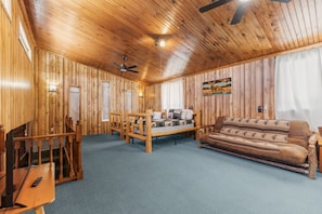 A log cabin interior with a wooden ceiling, a bed, a sofa, and a dining table.