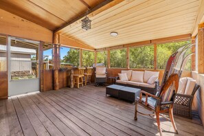 A covered outdoor area with wooden flooring, a sofa, chairs, and a small table. - Alpine Dream | ATV, Fishing & Mountain Escape (South Fork)