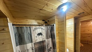 A wooden cabin interior with a shower curtain featuring a bear and arrows, a ceiling light, and a wooden floor. - Alpine Dream | ATV, Fishing & Mountain Escape (South Fork)