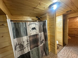 A wooden cabin interior with a shower curtain featuring a bear and arrows, a ceiling light, and a wooden floor.