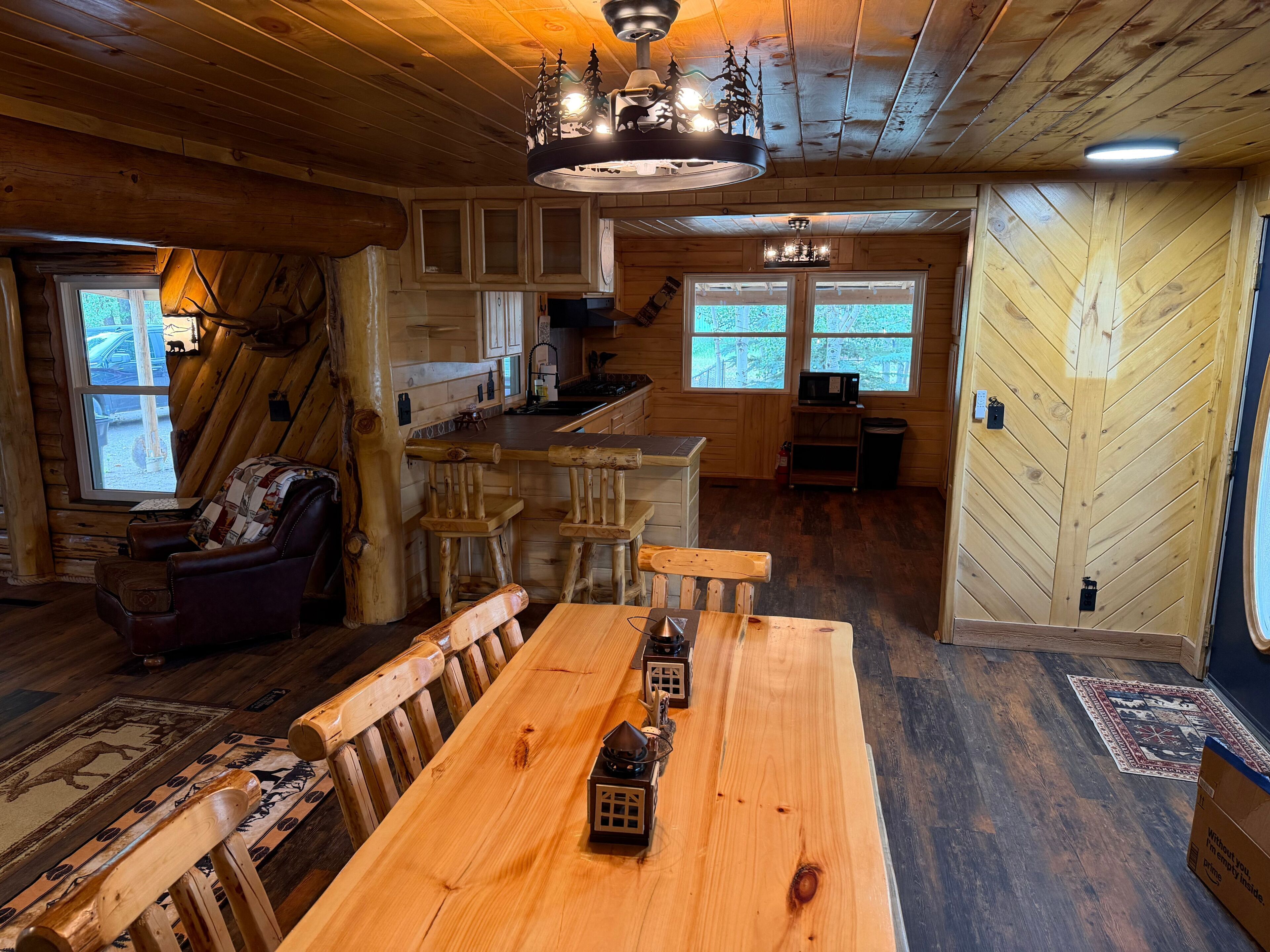 L’intérieur d’un chalet rustique comprend un coin repas, des murs en bois, une cuisine et une grande fenêtre.