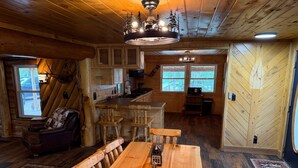 A rustic cabin interior with a dining area, wooden walls, a kitchen, and a large window. - Alpine Dream | ATV, Fishing & Mountain Escape (South Fork)
