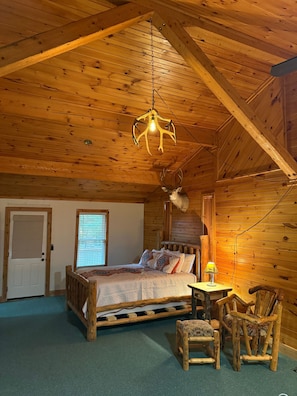 A wooden cabin interior with a bed, a table, and chairs.