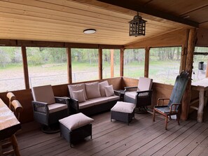 A covered outdoor seating area with wicker furniture, a wooden table, and a hanging lantern.