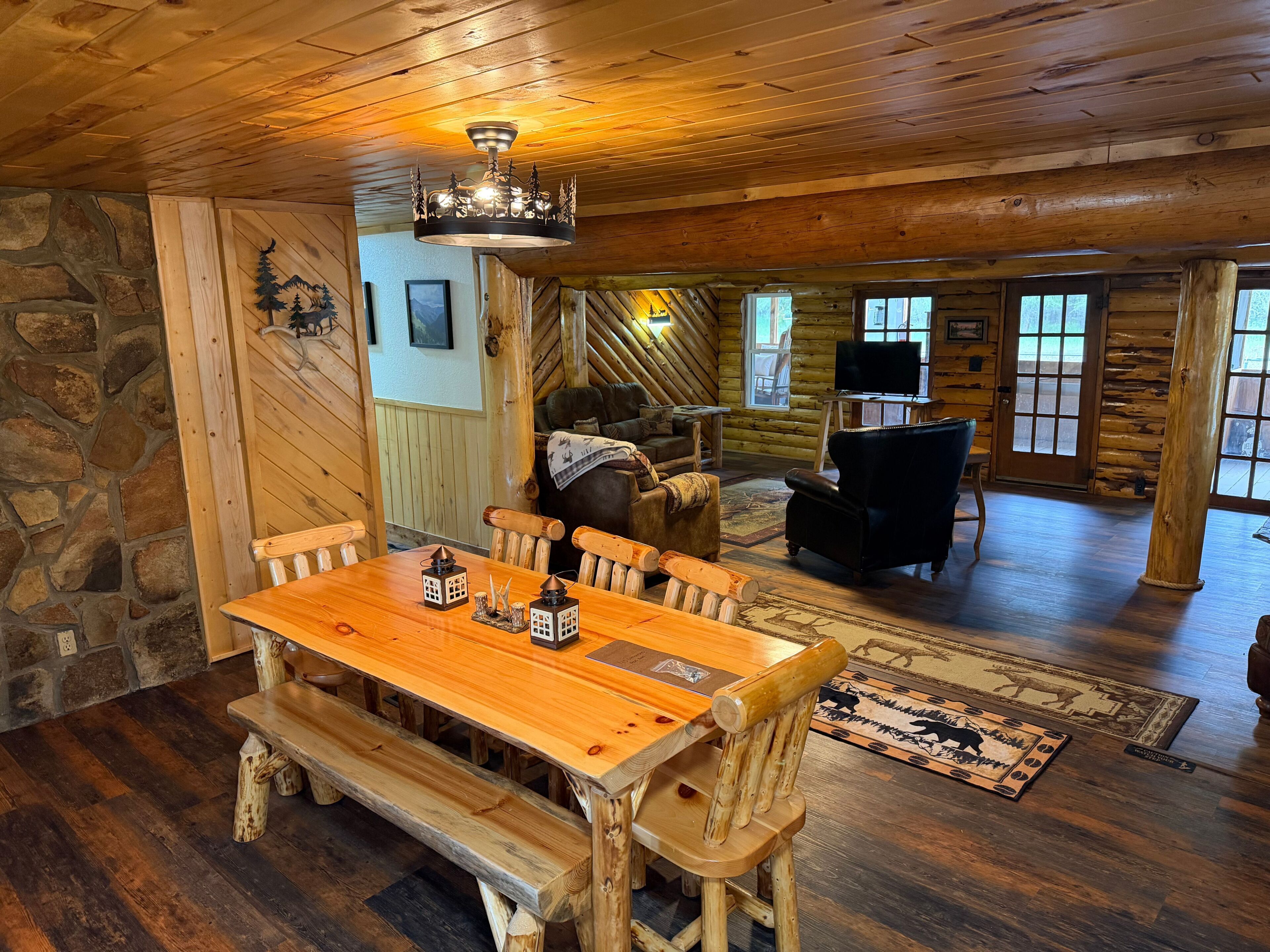 L’intérieur d’un chalet rustique en rondins de bois, avec une table à manger en bois, des bancs, une cheminée et un mur en pierre.