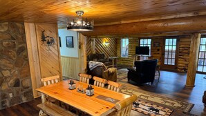A rustic log cabin interior with a wooden dining table, benches, a fireplace, and a stone wall. - Alpine Dream | ATV, Fishing & Mountain Escape (South Fork)