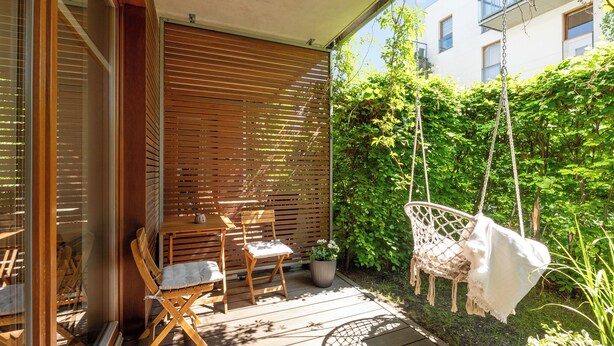 Um deck de madeira com móveis para área externa, um balanço suspenso e um jardim.