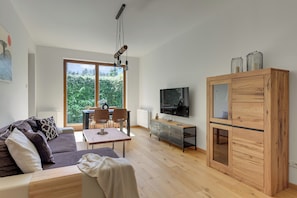 A modern living room with a sofa, dining table, chairs, a TV, and a wooden cabinet. - Nadmorski Dwór by Grand Apartments (Gdańsk)