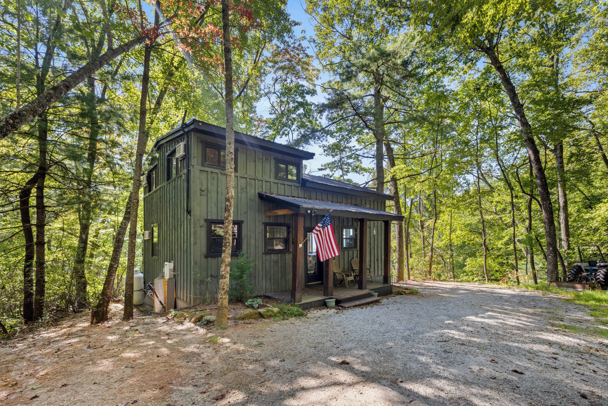 A rustic cabin with a porch, surrounded by trees.