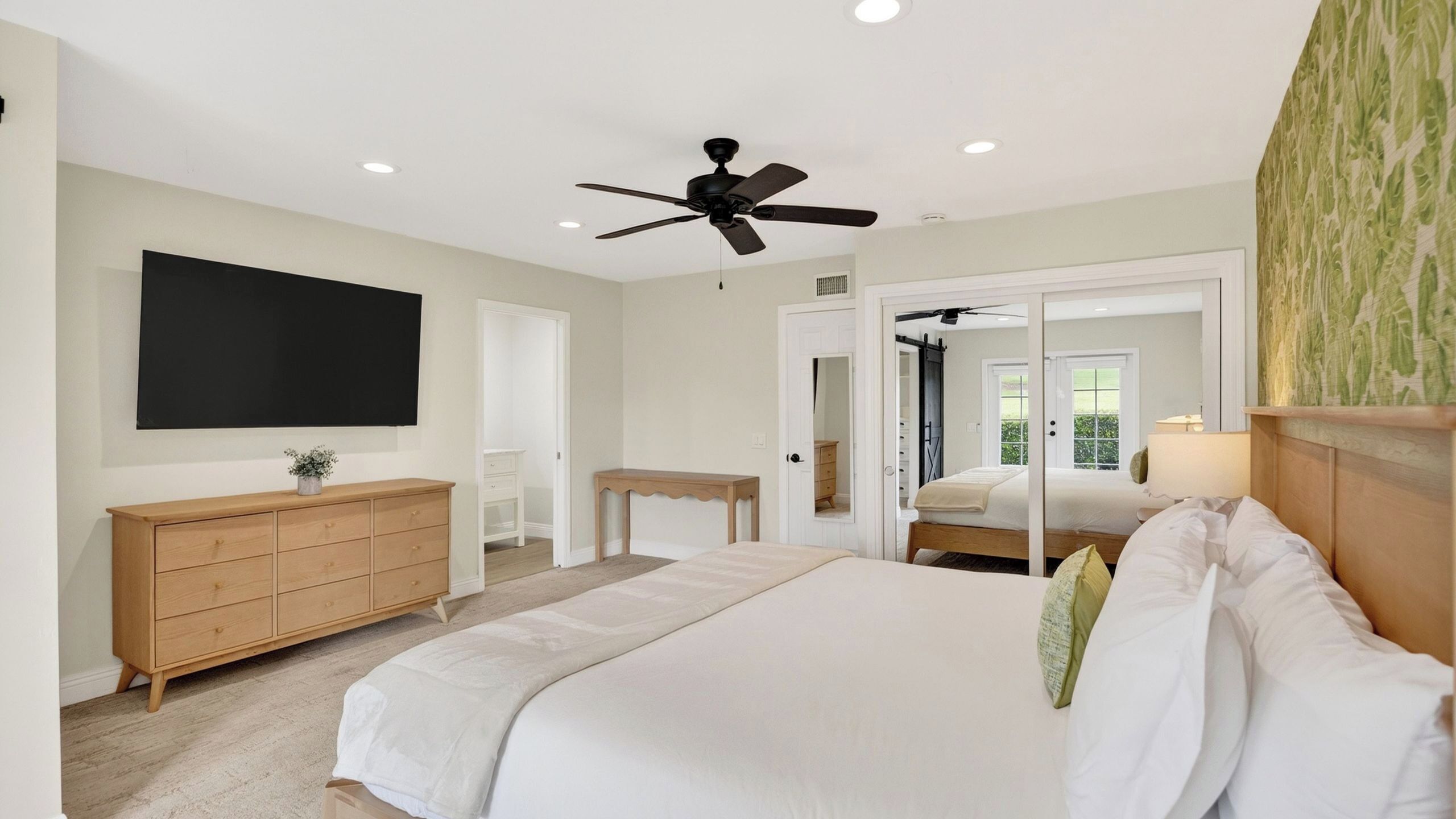 Um quarto com cama, ventilador de teto, televisão, cômoda, escrivaninha e espelho.