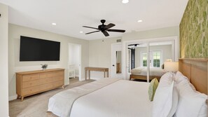 A bedroom with a bed, a ceiling fan, a TV, a dresser, a desk, and a mirror.