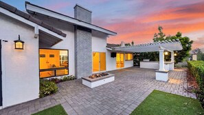 Ein modernes Haus mit Terrasse, Feuerstelle und einer Pergola.