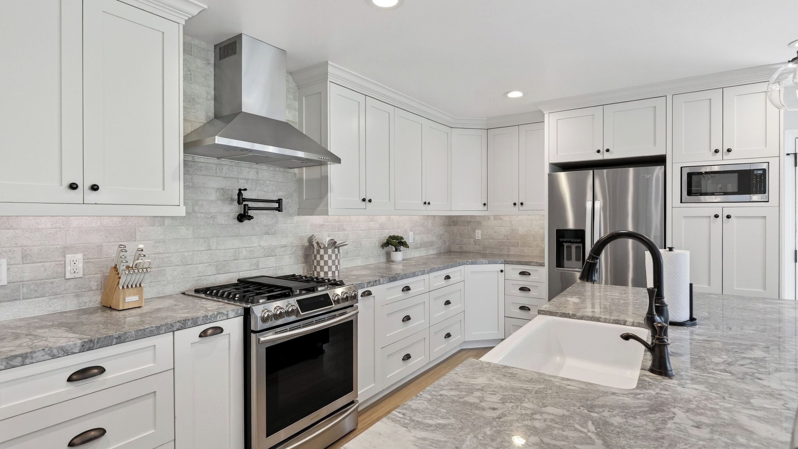 Una cocina moderna con armarios blancos, estufa de acero inoxidable, horno empotrado, refrigerador de acero inoxidable y microondas.