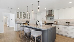 Een moderne keuken met witte kastjes, een groot eiland met barstoelen, hanglampen en een roestvrijstalen afzuigkap.