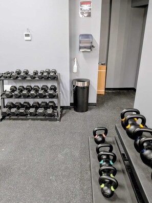 A gym with multiple rows of dumbbells, a trash bin, and a water dispenser.