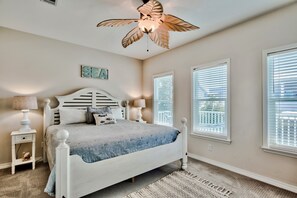 Ein Schlafzimmer mit einem Bett, einem Deckenventilator und zwei Fenstern.